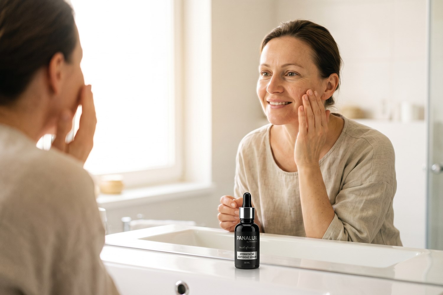 Žena nanáší hydratační peptidové sérum Panakeia před zrcadlem v ranním světle